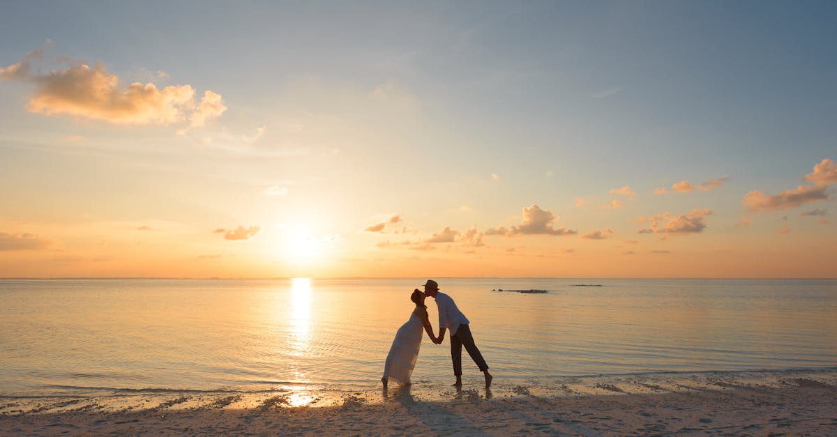 A couple kisses on a tropical beach at sunset in the Maldives, showcasing love and serenity.