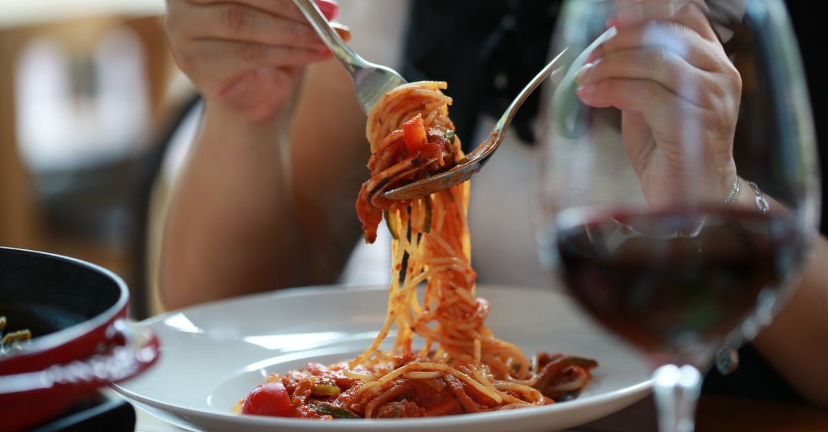 A close-up of a woman enjoying a spaghetti meal with a glass of wine in a restaurant setting.