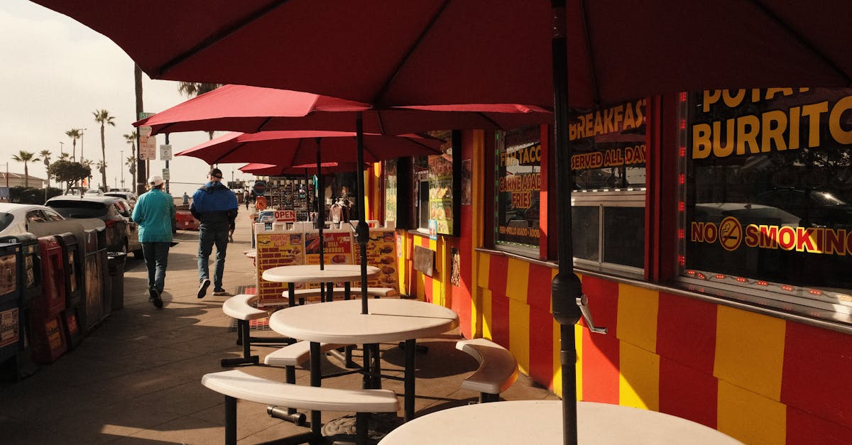 Urban outdoor restaurant seating featuring red umbrellas and street view.
