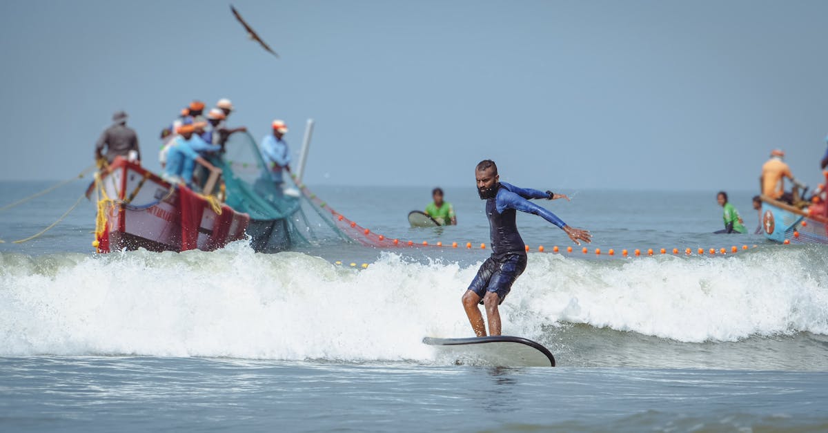 Man surfing near fishing boats on a sunny ocean day, showcasing water sport activity.