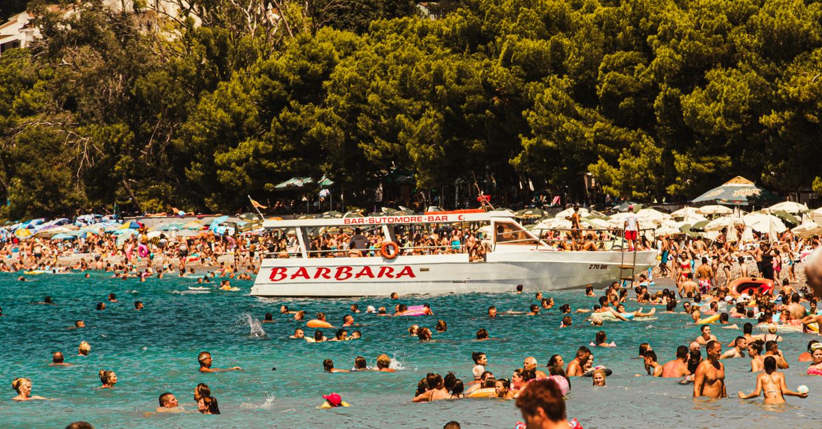 Vibrant summer day at a packed beach in Bar, Montenegro with a boat and swimmers enjoying the sun.