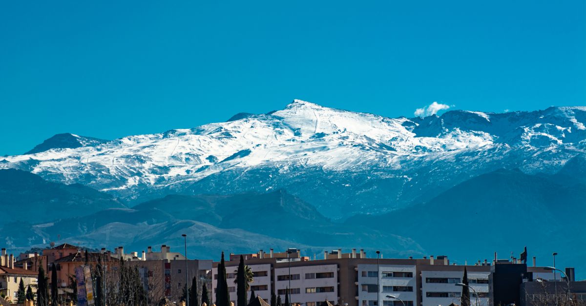 Panoramic view of snowy Sierra Nevada mountains towering over Granada's urban landscape.