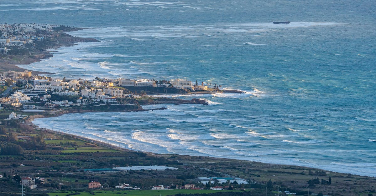 Aerial view of a coastal town with waves crashing along the shoreline, showcasing urban and natural landscapes.