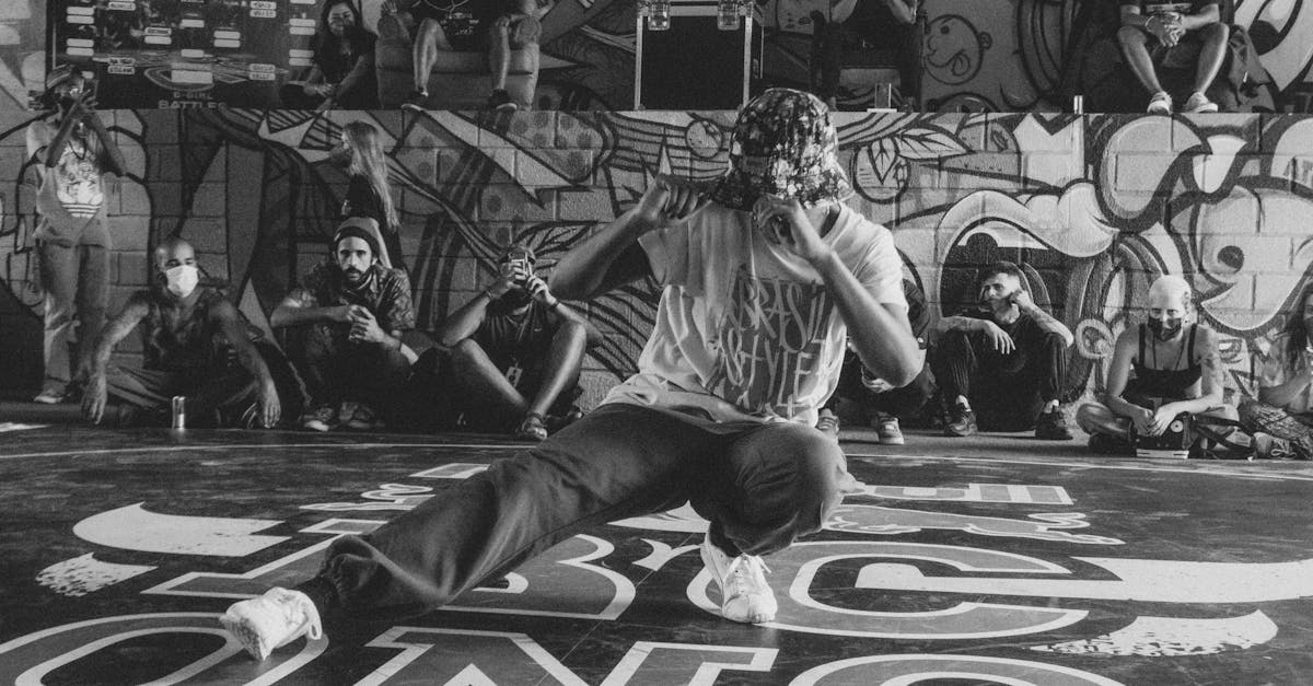 A breakdancer performs energetically in front of a graffiti wall, surrounded by an audience.