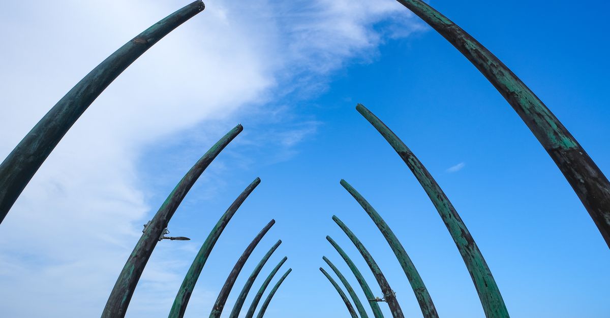 Artistic metal sculpture arcs beneath a vibrant blue sky with clouds, creating a dramatic effect.