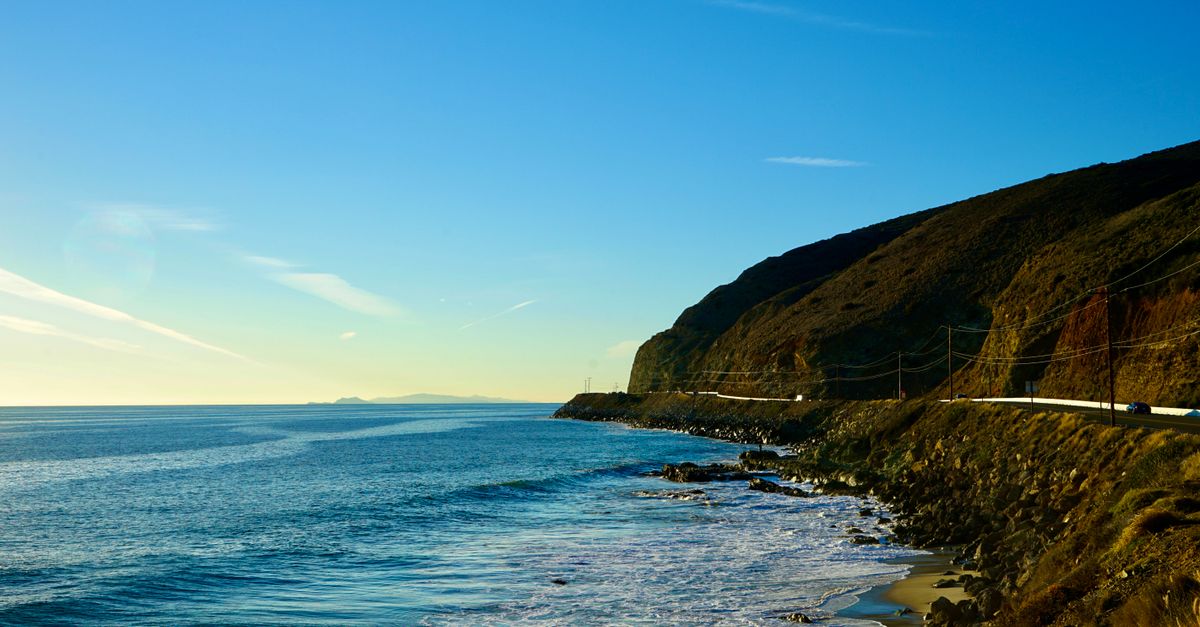 Beautiful coastal view in California with serene ocean waves and a clear blue sky at sunset.