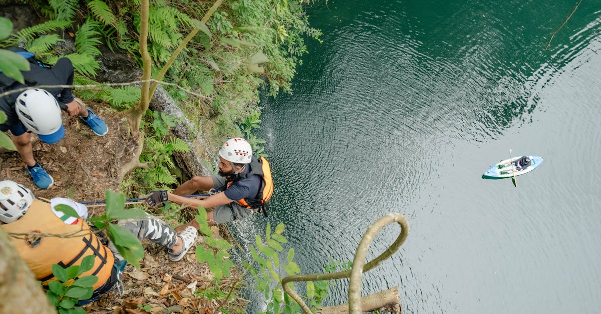 Group of climbers rappelling down a cliff face over a serene lake, enjoying an adventurous sport.