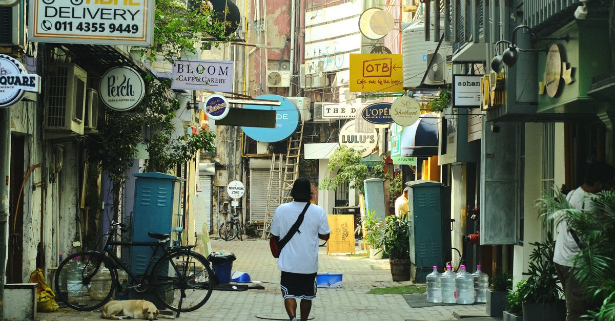 Man walking along a vibrant street with shop signs, bicycle, and resting dog.