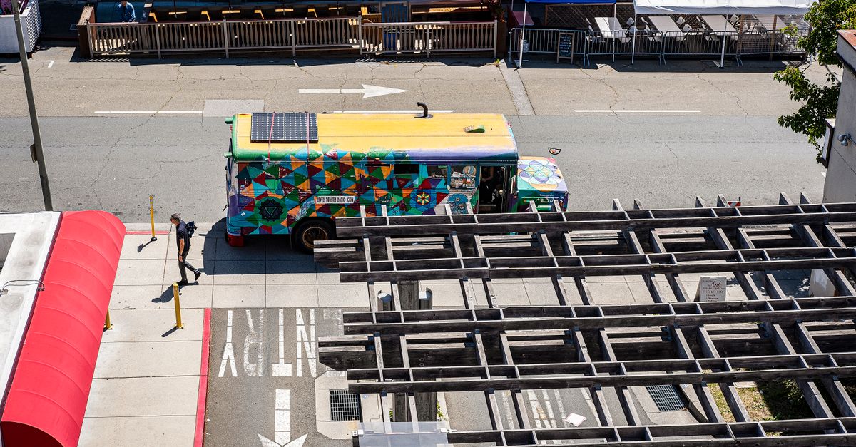 A vibrant, artistic bus parked on a city street, viewed from above on a sunny day.