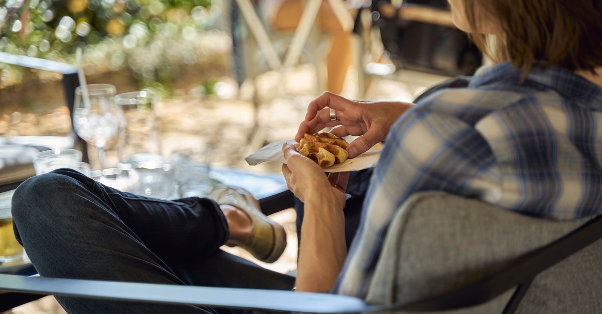 Person in plaid shirt enjoying food outdoors, seated comfortably with blurred background.