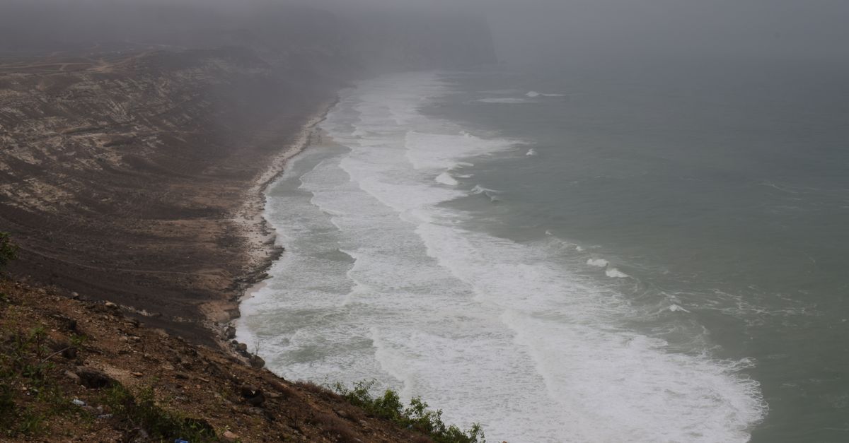 Dramatic view of a foggy coastline with waves crashing on the shore.