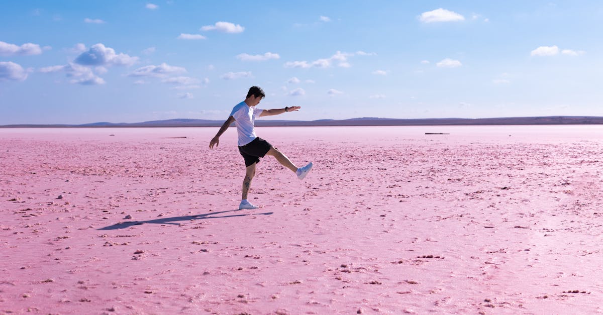 A man strolls across a stunning pink salt flat beneath a vibrant blue sky, offering a unique scenic view.