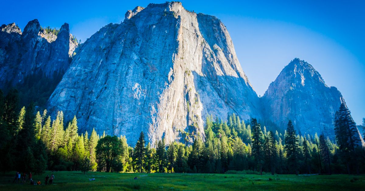 Breathtaking view of Yosemite mountain peaks surrounded by lush greenery under clear blue skies.
