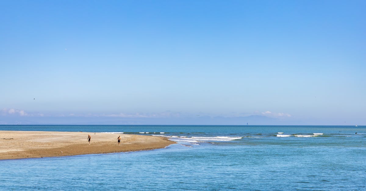 Peaceful beach scene with two people walking along the shoreline under a clear blue sky.