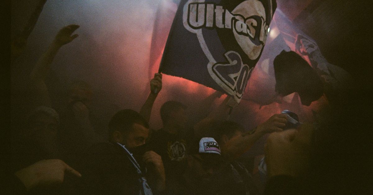 A lively crowd of sports fans waving flags amidst smoke, creating an intense atmosphere.