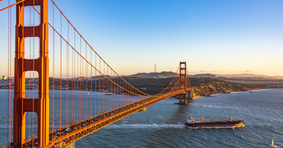 Iconic view of Golden Gate Bridge in San Francisco at sunset with ships passing, under a clear sky.