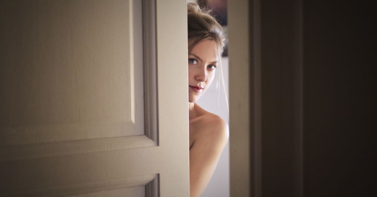 A woman peeks through a slightly opened door, creating a mysterious and intriguing atmosphere.