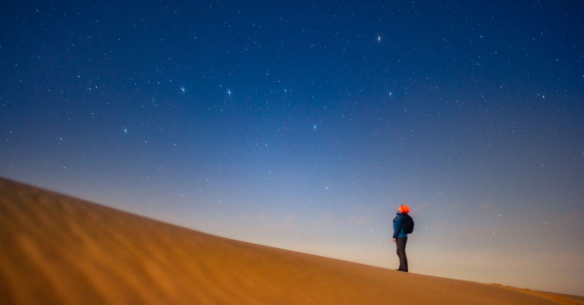 A lone person gazing at the starry night sky from a sand dune, evoking tranquility and wonder.