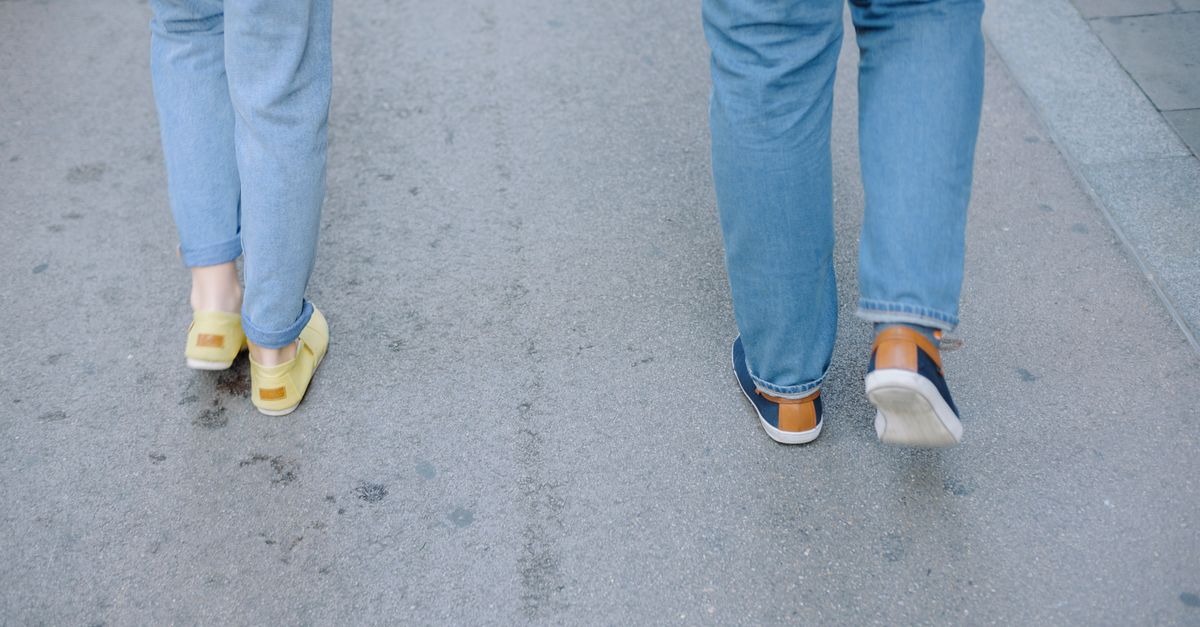 Two people walking casually on a city pavement in jeans and sneakers.