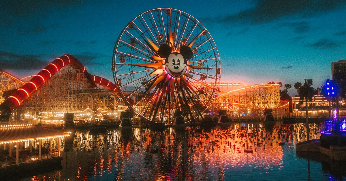 Stunning view of a brightly lit Ferris wheel at a theme park during sunset, reflecting on the water.