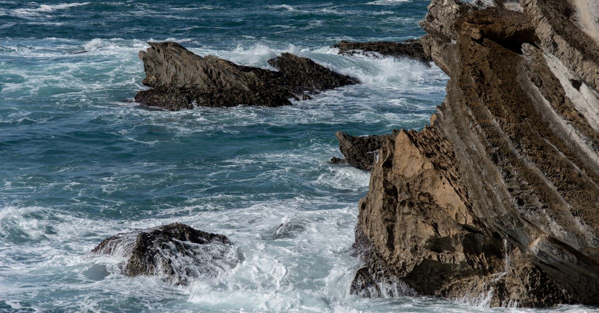 Eroded coastal rocks with waves crashing against them, depicting raw nature.