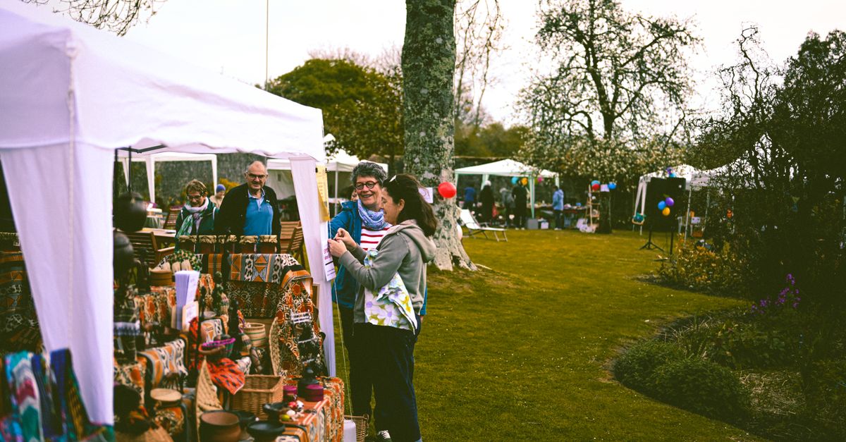 A lively outdoor market with people browsing stalls and tents in a park setting.
