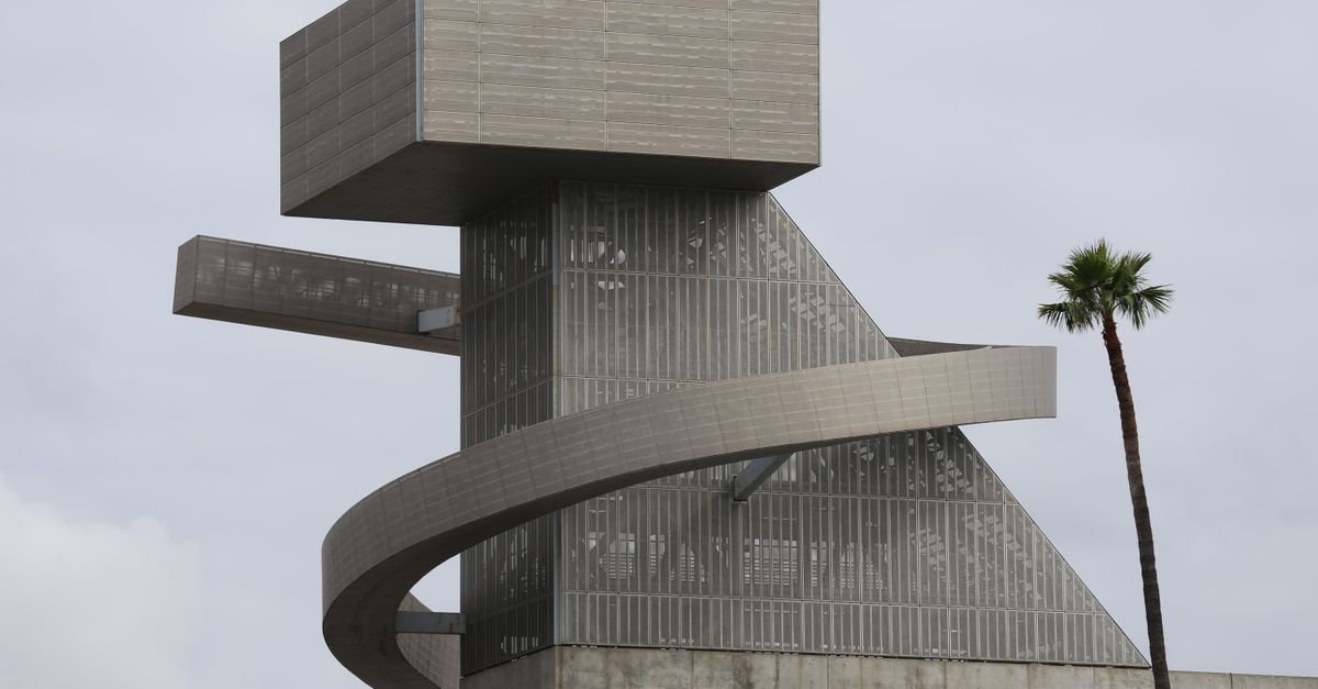 Modern architectural structure with a spiral design under cloudy skies and palm trees.