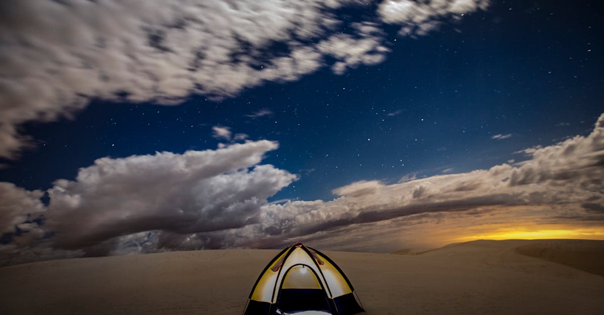 A solitary tent under a starry night in a vast desert, with dramatic skies and distant sunset glow.