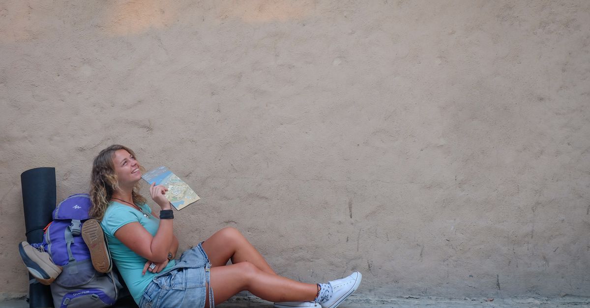Smiling female traveler sitting by a wall with a map, enjoying a moment of relaxation on her journey.
