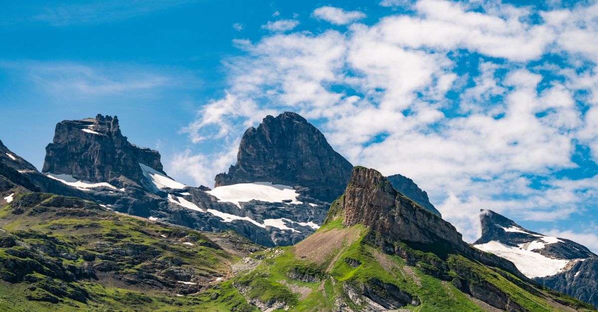 Stunning view of rugged mountain peaks with snow patches and vibrant green slopes under a bright blue sky.