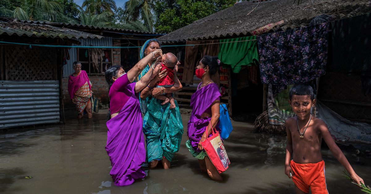 Women and children wade through floodwaters in a village, showcasing resilience amidst adversity.