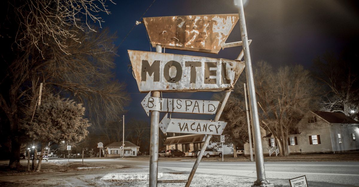 A vintage motel sign captured during nighttime on an empty urban street.
