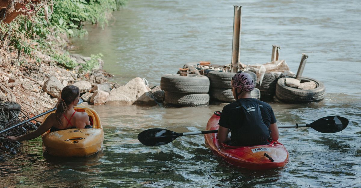 Two people canoeing on a calm river, engaging in an outdoor activity.