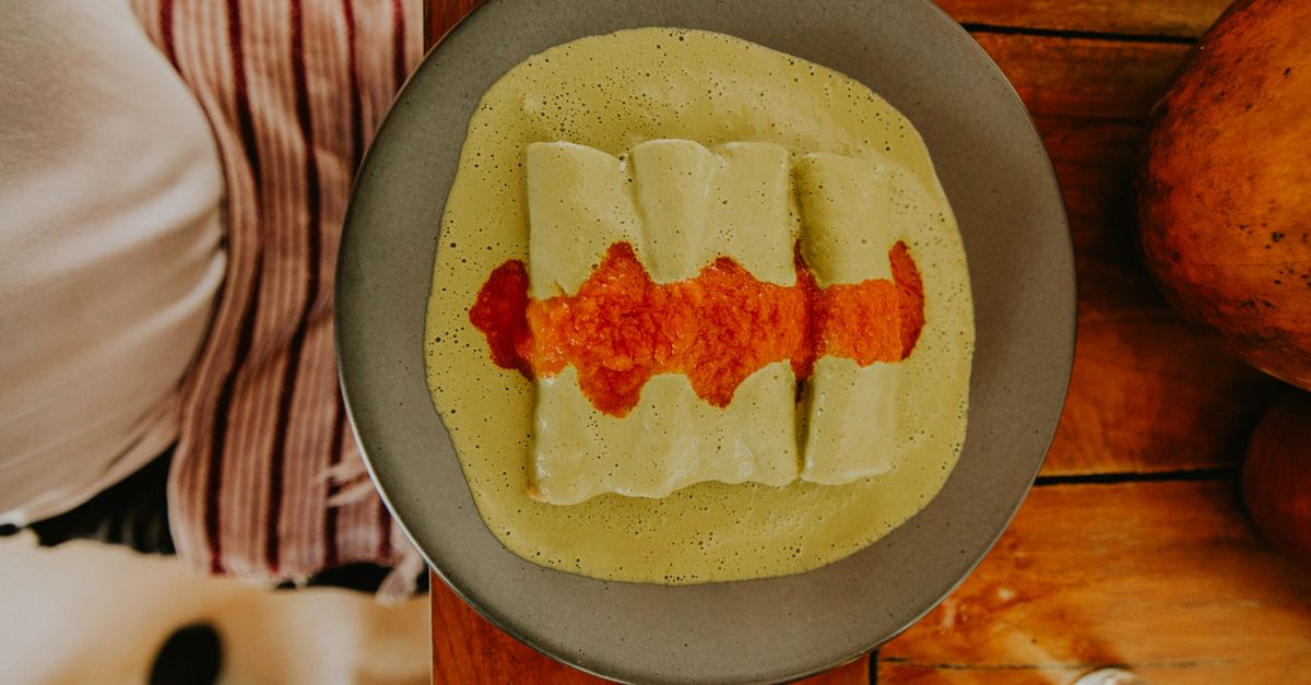 Top-down view of enchiladas with green sauce and red salsa on a rustic wooden table.