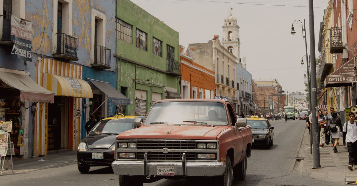 A vibrant street scene captures the essence of Heroica Puebla de Zaragoza with colorful buildings and busy traffic.