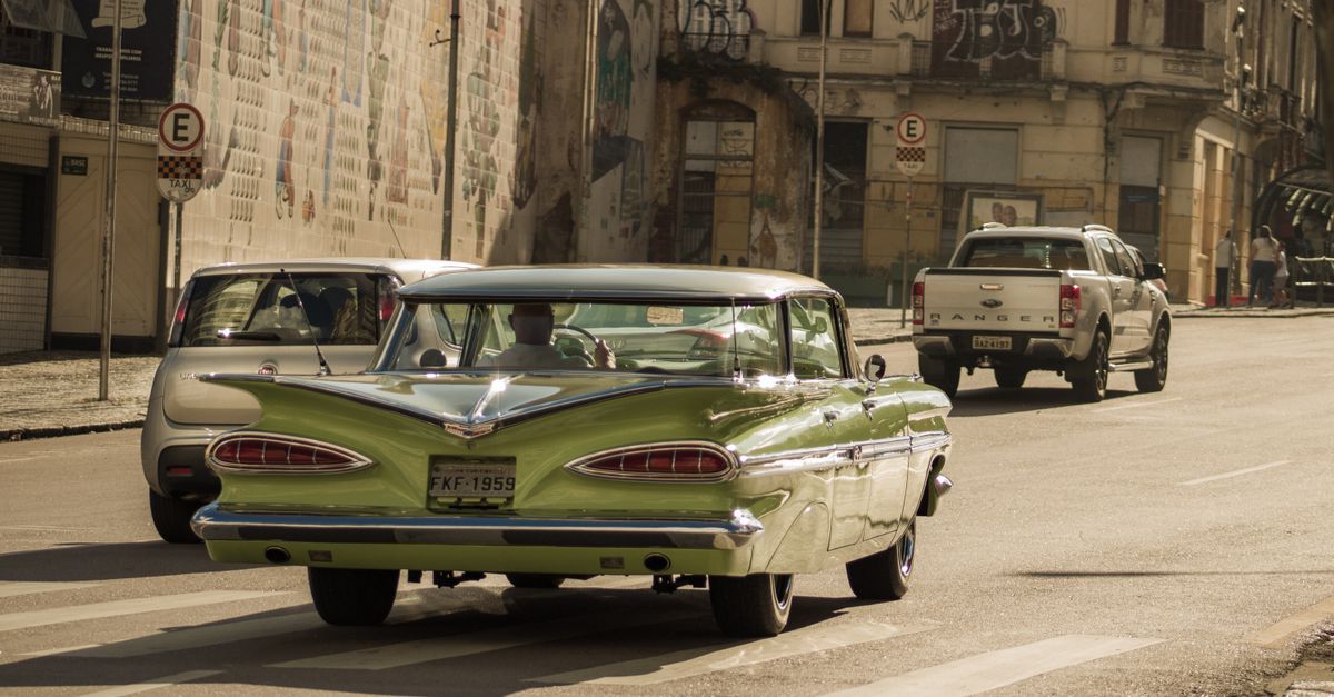 Classic green Chevrolet Impala cruising down a city street lined with historic buildings.