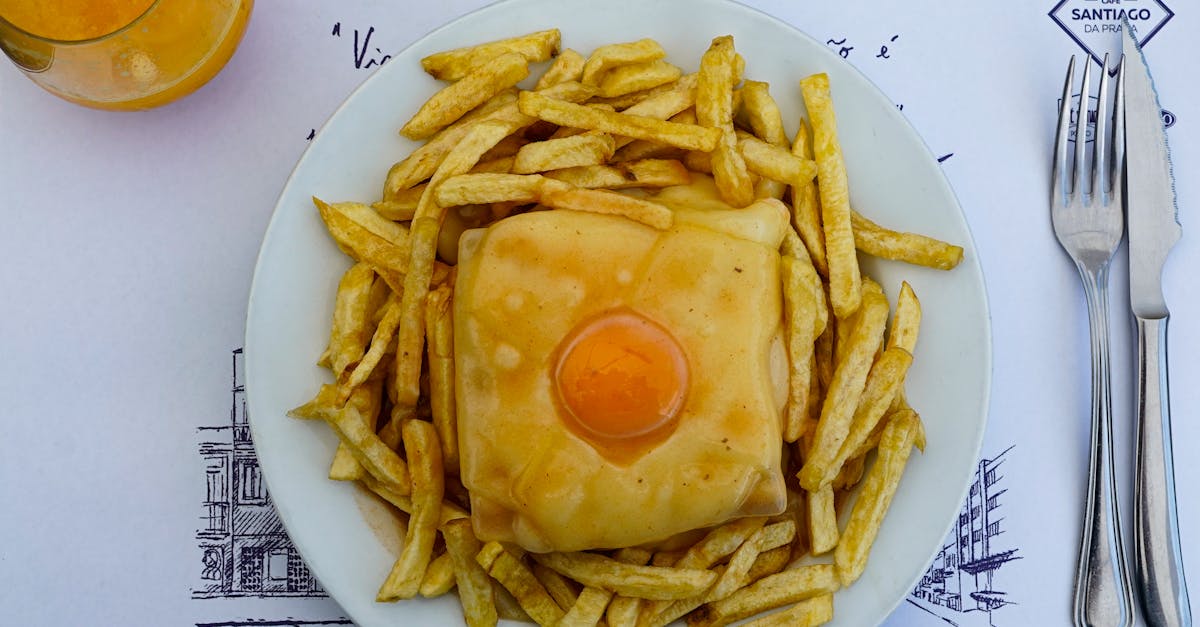 Tasty Portuguese francesinha sandwich topped with egg, surrounded by crispy fries and fresh juice.