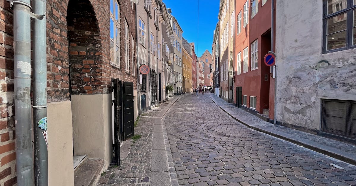 A picturesque cobblestone street in Copenhagen's old town, featuring colorful buildings and a bright blue sky.