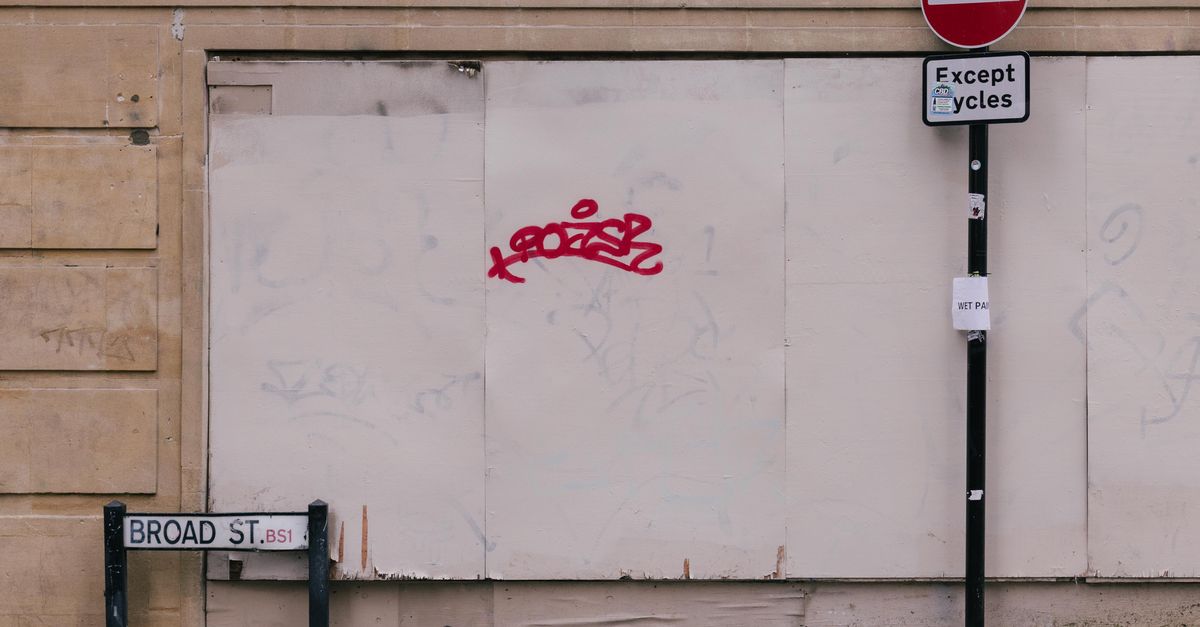 Street view featuring a no entry sign, graffiti, and signs on a city wall.