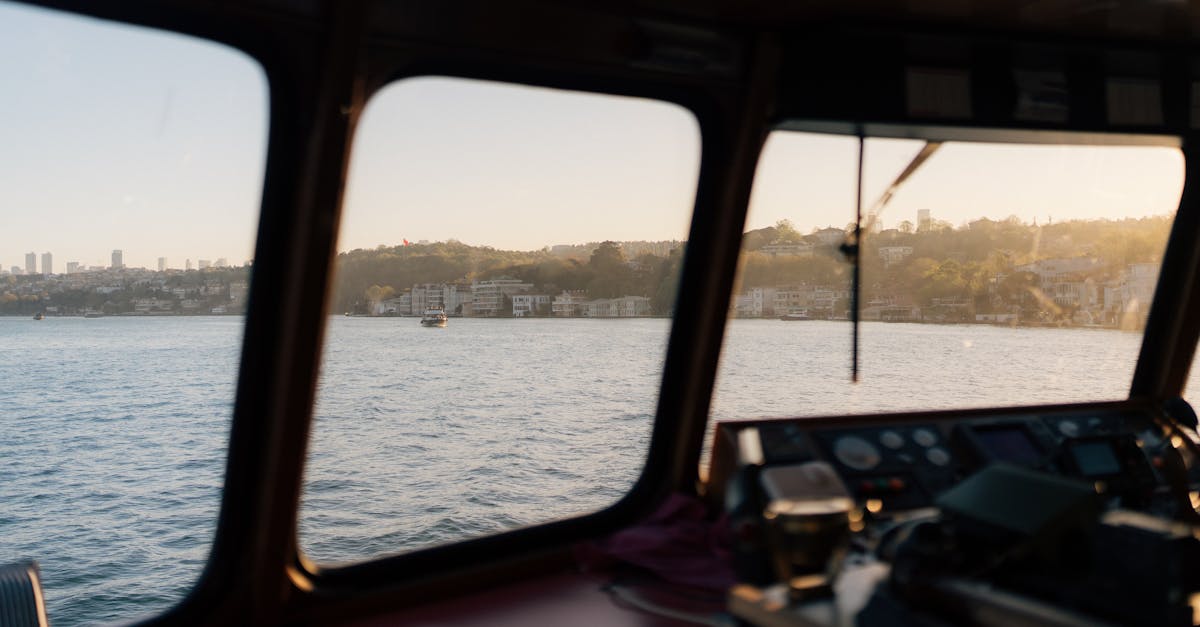 View from a ship bridge overlooking the water and urban coastline at sunset.