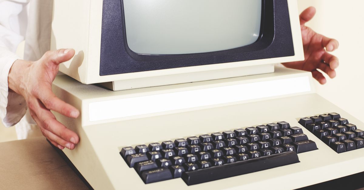 A vintage computer with a classic CRT monitor and keyboard, being held by hands.