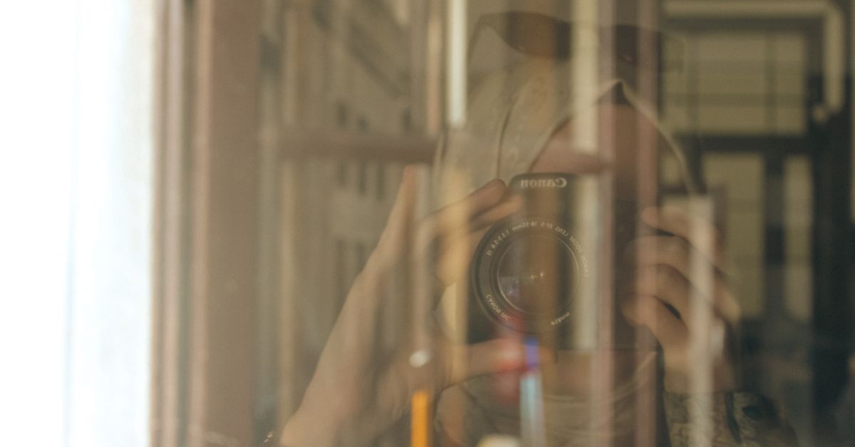 A reflective portrait capturing a photographer with a camera through a glass pane, blending interior and exterior views.