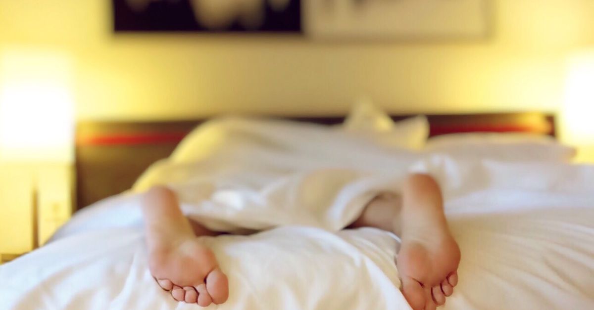 A person relaxing on a bed with feet under white sheets, conveying serenity.