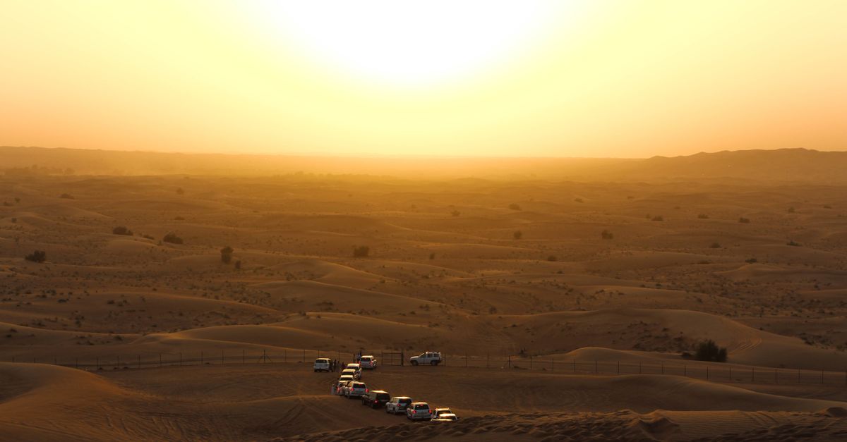 Off-road vehicles traverse the desert dunes under a warm golden sunset, ideal for adventure travel.
