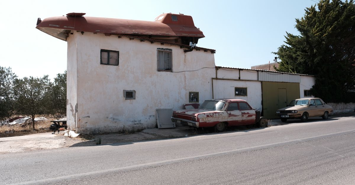 Unique house with a car on the roof and vintage cars parked outside on a sunny day.