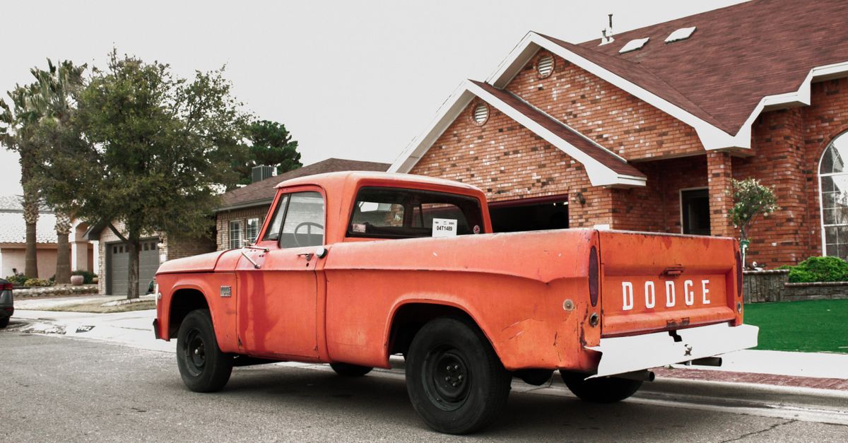 Old red Dodge truck parked in a quiet suburban neighborhood street.