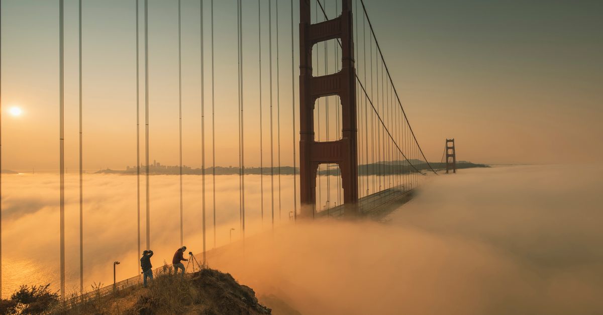 Dramatic view of the Golden Gate Bridge enveloped in fog during sunrise with silhouetted photographers.