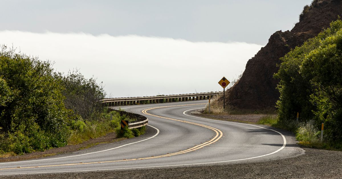 A scenic winding road through lush countryside with clear skies, inviting exploration.