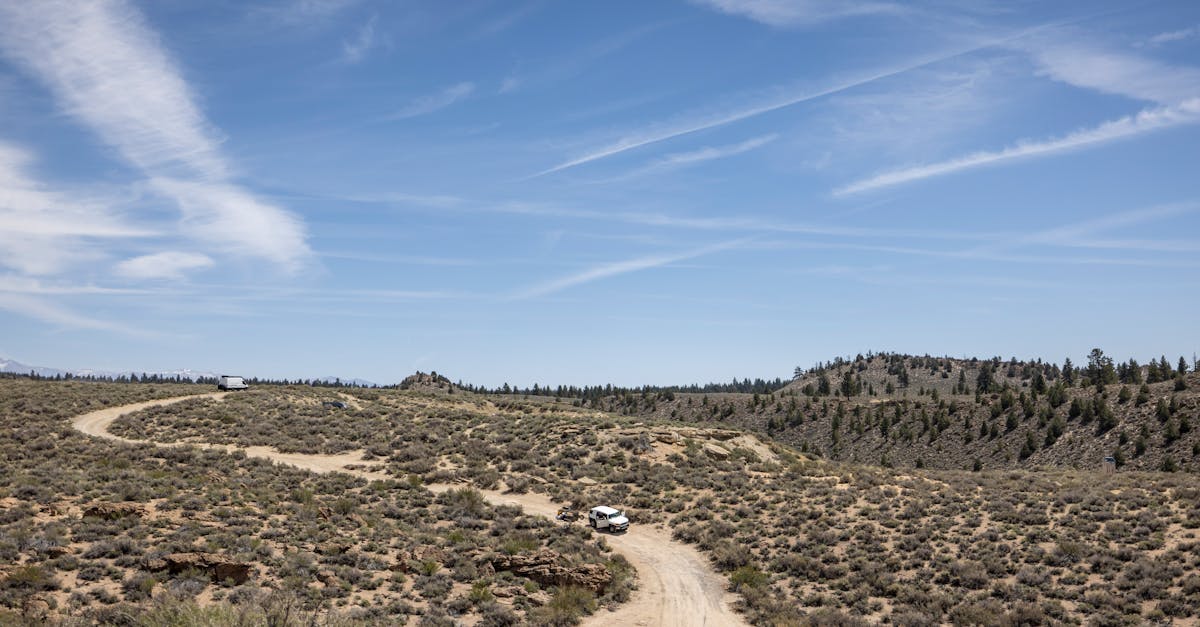 Scenic desert landscape with off-road vehicles on a dirt trail under a clear sky.