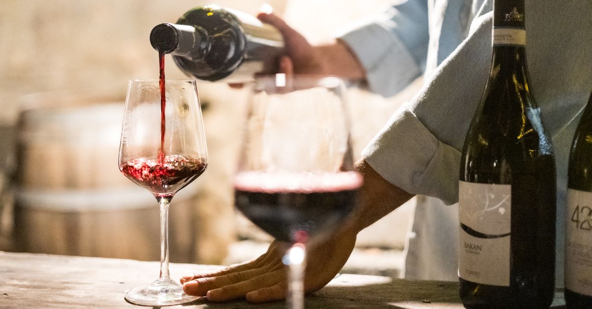 A person pouring red wine into a glass in a rustic, cozy wine bar setting.